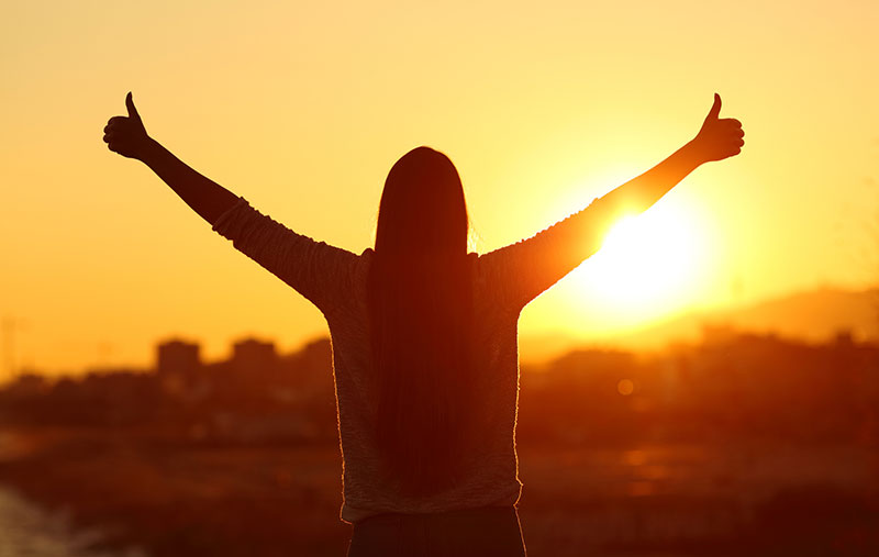 Woman giving thumbs up while looking at sunrise
